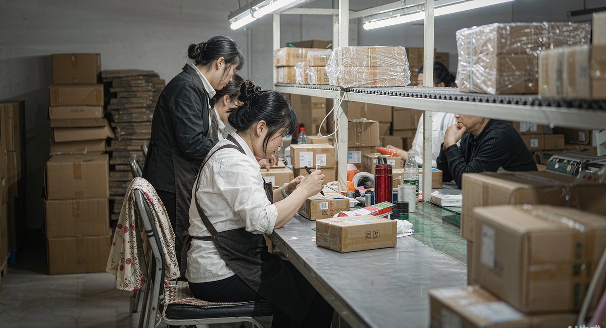 打包区里工人给纸箱贴标装箱,传送带上码满待发的包裹